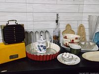 Photo showing a variety of kitchen collectibles on a white wood background including baking pans, mixing bowls, a Land O Lakes bottle dispenser and cookie molds.
