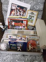 View of the lot showing baseball storage boxes, framed memorabilia, packaged figures, and collectible baseball items on a patterned couch.