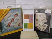 Front view of two sealed needlepoint kits and a Singer accessories box.
