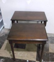 Two wooden nesting tables shown side by side on floor, dark brown finish, straight legs, rectangular tops.