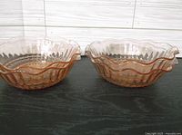 Two pink Depression glass bowls side by side showing scalloped rim and textured patterned sides.
