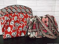 Red Vera Bradley handbag with white and black floral pattern next to pink quilted Vera Bradley handbag