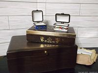 Three jewelry boxes stacked; one large dark brown wooden box and two smaller decorated hinged trinket boxes visible