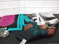 Three vintage silk scarves layered on a surface with metal scarf clips and pins arranged on top.