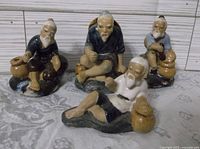 Four vintage Asian mud figurines depicting elderly men in different poses with bags, photographed on fabric background.