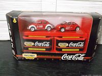 Front view of the boxed Matchbox die-cast set showing two VW Beetle cars and two Coca-Cola trailers inside transparent packaging.