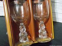 Two clear glass goblets with Winnie the Pooh figurine stems shown side by side, inside original box.