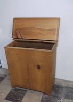 Front view of wooden storage hamper with lid open showing interior and wood grain.