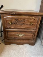 Front view of one bedside table showing two drawers with carved wood details and brass hardware.