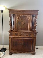 Front view of antique mixed wood china cabinet showing closed upper and lower doors, intricate wood carvings and vertical turned columns on sides.