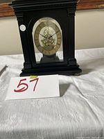 Photo showing front view of the Bombay Company black mantel clock with skeleton dial and Roman numerals on a white cloth-covered surface.