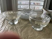 Etched glass fruit bowls and plates on table with cream and sugar set in background