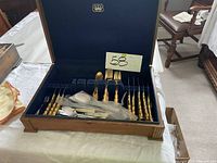 Gold Regency flatware set in open wooden box showing gold forks, spoons, knives with ornate handles.
