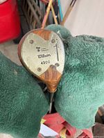 Close-up of a Wilson A300 custom wooden driver head showing wear and wooden finish, with green head cover