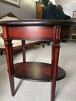 Side view of the oval wooden table showing the legs, skirt, and lower shelf beneath the tabletop.
