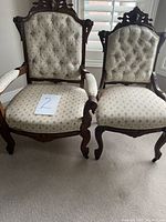 Two Queen Anne style oak chairs placed side by side showing differing sizes and armrest presence, tufted floral upholstery, and intricate wood carvings