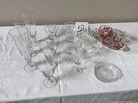 Full view of the set on white tablecloth showing cream and sugar set in ruby red with assorted clear glassware including stemmed glasses and tumblers