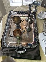 Silver plated tea tray with two cups and two candlesticks on top, tray has ornate handles and detailed pattern