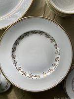 Top and front view close-up of white plate with gold wheat pattern around the inner rim and gold edge trim, part of Albany Wheat gold pattern china set.