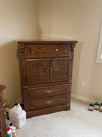 Front view of medium-brown wooden tallboy dresser with multiple drawers and two-door cabinet section, showing hardware, carved doors, and overall structure.