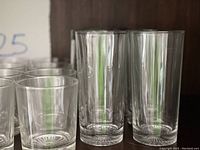 Close-up of tall highball glasses, clear glass, with vintage style design, beside small glasses in cabinet.