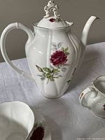 Photo of Royal Albert Canadian Rose teapot, cream jug, and part of saucer and teacup on white cloth background