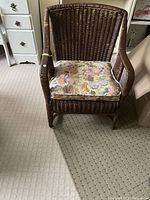Front view of brown wicker chair with floral seat cushion on carpeted floor.