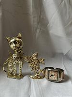 Photo of cat-shaped earring holder with rhinestone accents, floral earring holder, and silver-tone wristwatch.