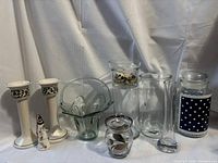 Photo of various candle holders, sugar dish, decorative jars, and glass vases arranged on a draped white cloth background.