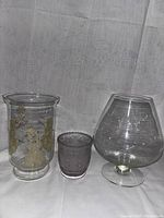 Three glass vases including a snowman design vase, small frosted vase with floral pattern, and large clear pedestal vase.