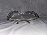 Side view of the clear glass triangular candy bowl showing scalloped edges and three small square feet.