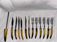 Full set of 13 cutlery pieces laid out on white cloth including knives, forks, and sharpening rod.