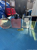 Four Chanel perfume bottles arranged on blue surface with natural light showing full and partial liquid contents.