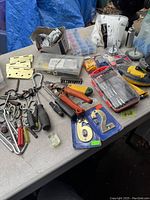 Wide view of assorted tools, metal hardware, electrical connectors, and number plates on a tabletop.