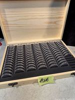 Open wooden box showing multiple rows of clear plastic coin holders arranged in foam insert inside the box.