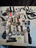 Overview of 30 assorted men's watches in various styles, bands, and conditions spread on table.