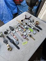 Photo showing a wide assortment of men's watches laid out on a table, featuring a variety of band types and dial colors.