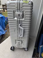 Front view of the silver suitcase showing combination locks, handle, and one wheel.