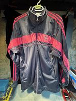 Front photo of the Adidas jacket showing black body with red chest stripe, red shoulder stripes, zipper and logo on chest.