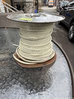 Side view showing the coiled white insulated 14-2 Romex electrical wire wound around the metal spool.