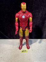 Front-facing photo of the Ironman Avengers action figure standing upright on a flat surface against a black background. The figure is about 11.5 inches tall with red and gold coloring and a blue arc reactor on the chest.