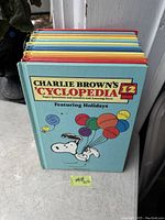 Front cover of Charlie Brown's Cyclopedia Volume 12 featuring Snoopy with holiday balloons on light blue background.