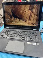 Photo of Lenovo laptop powered on showing lock screen with scenic background, keyboard, touchpad, and brand labels.