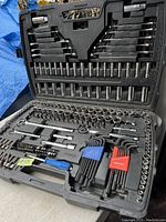 Open black plastic case showing full set of sockets, wrenches, hex keys, screwdriver bits, and a blue handled tool, arranged neatly.