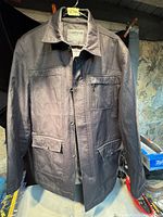 Full front view of the brown men's jacket showing the collar, zipper, button pockets, and embossed Falcon logo on the chest pocket.