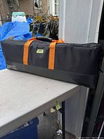 Black rectangular badminton racket case on a white surface, orange handles visible.