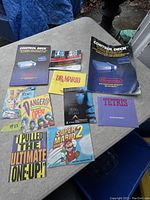 Photo showing 12 vintage Nintendo instruction and game booklets spread out on a table. Titles include Control Deck, Dr. Mario, Tetris, Super Mario Bros 2, Total Recall, and others.