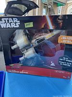Front view of the boxed Star Wars Air Hogs X-Wing toy showing the product through the clear window with branding and flying range details.