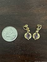 Photo showing the pair of gold tone amethyst colored screw back earrings placed next to a Canadian quarter for size comparison.