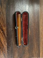 Glass holder inside open black hinged case with red velvet lining, placed on a wooden surface